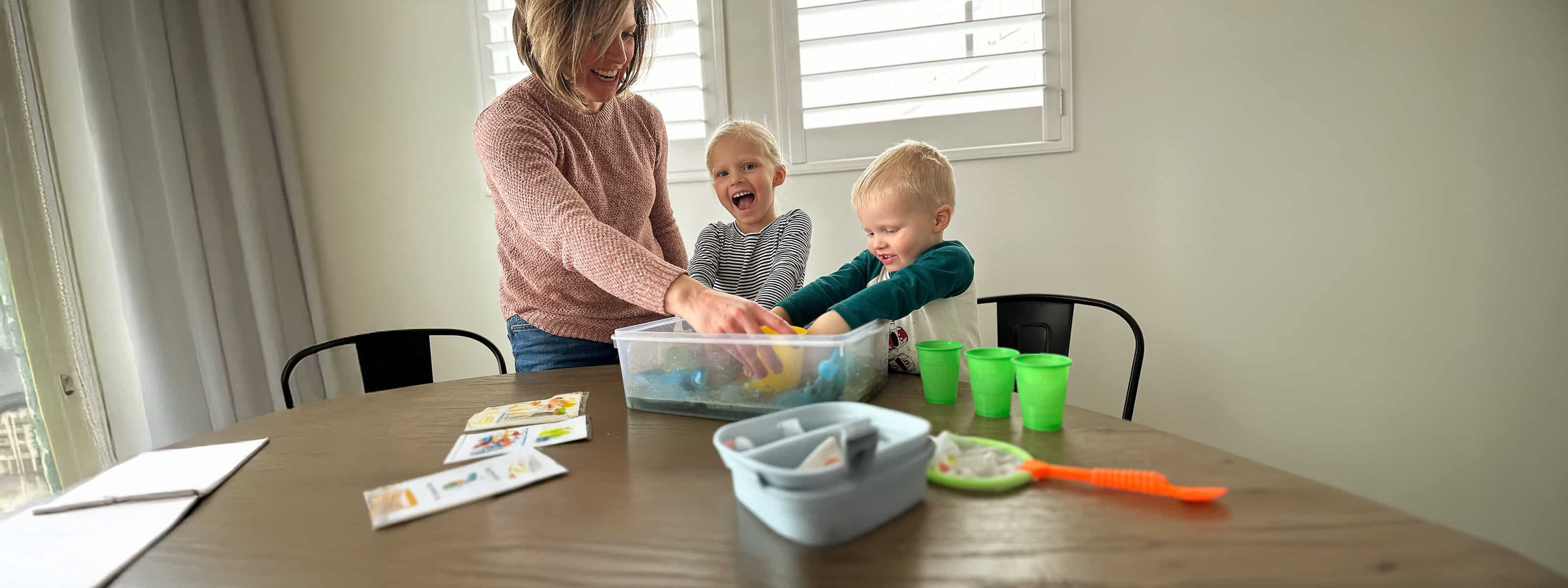 Engaged mom and kids enjoying sensory play with colorful sand in a bright room.